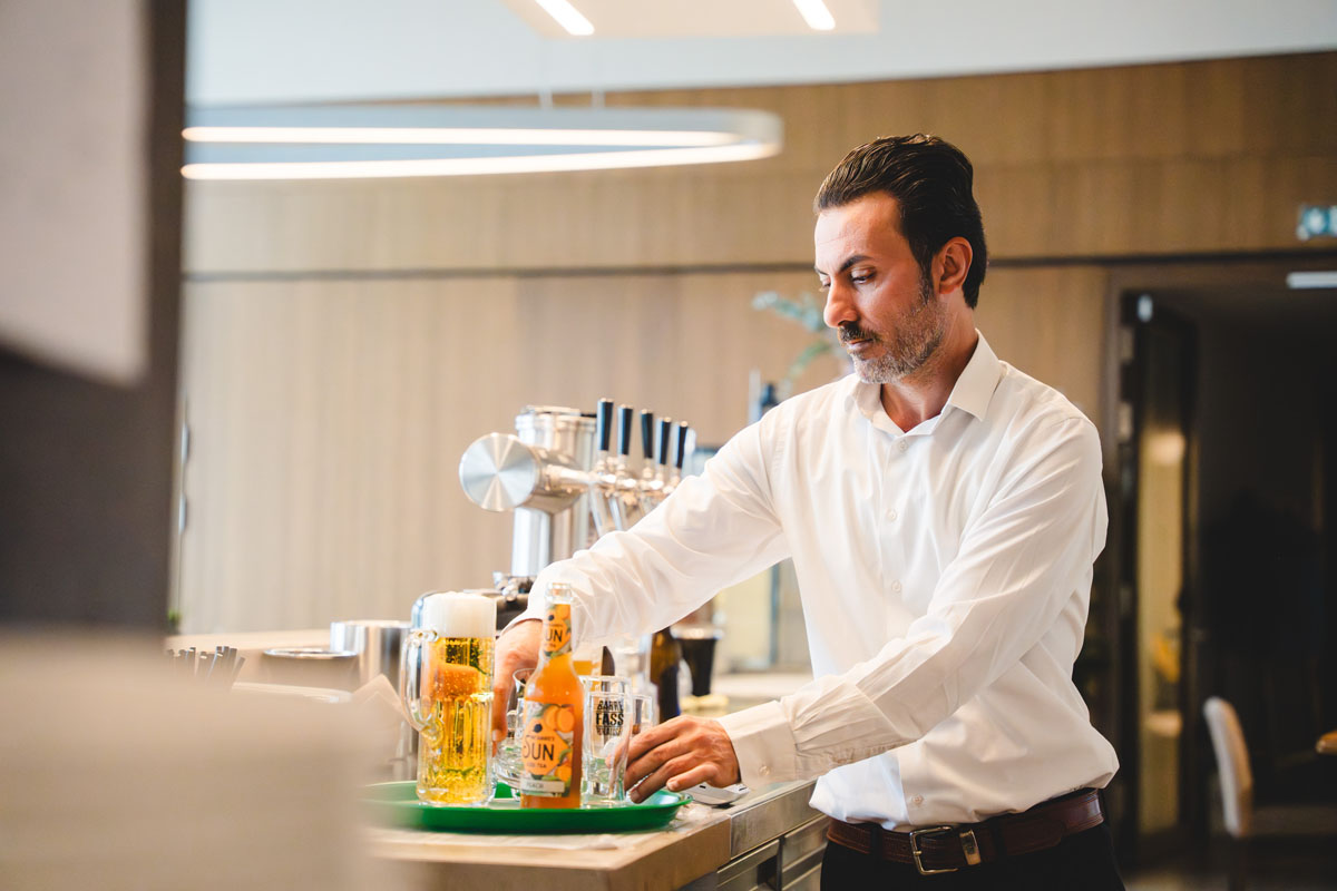 Barkeeper im Bella Vista bereitet Getränke an der Zapfanlage vor – Bier, Saft und Shots auf einem Tablett