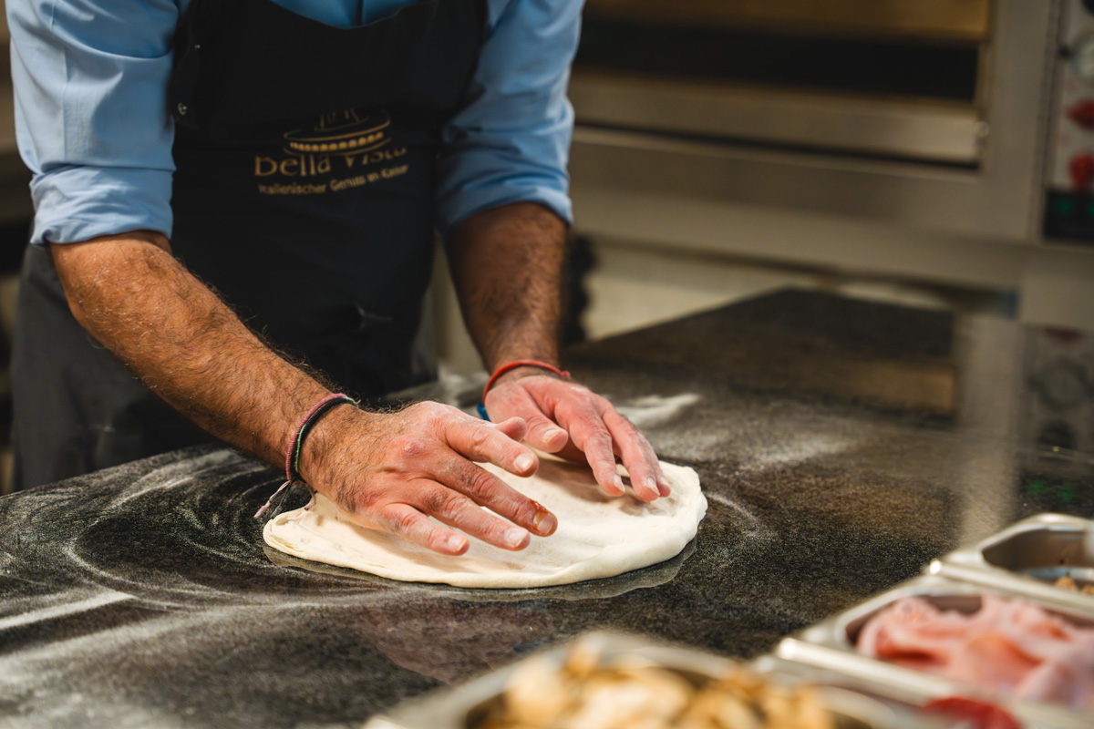 Koch in Bella Vista-Schürze knetet Pizzateig auf bemehlter Arbeitsfläche